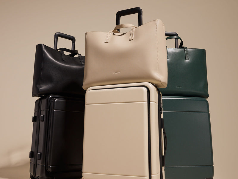 Trio of CALPAK Haven Laptop Totes stacked on matching Hue Front Pocket Carry-On Luggages