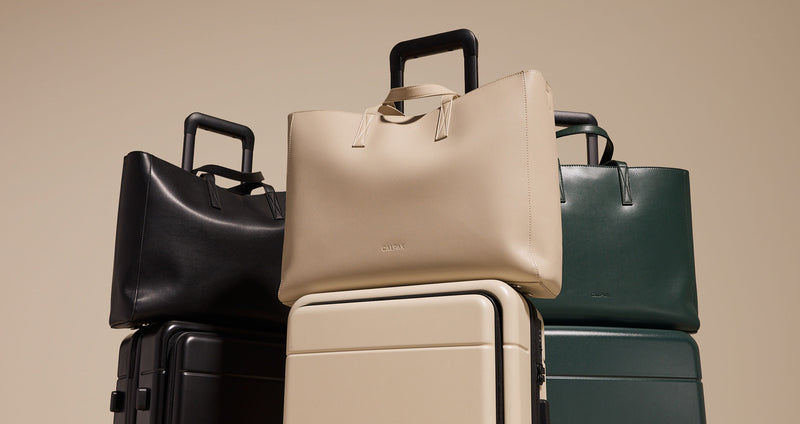 Trio of CALPAK Haven Laptop Totes stacked on matching Hue Front Pocket Carry-On Luggages
