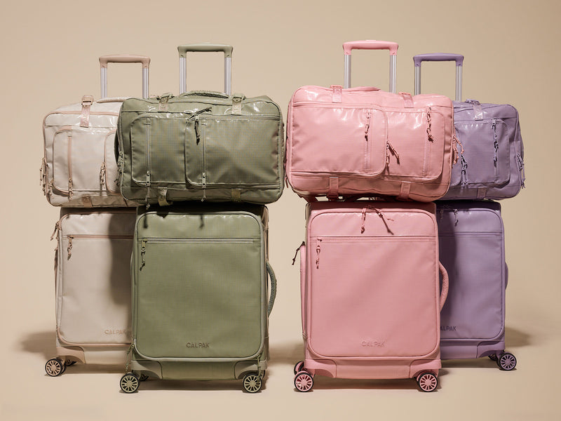 Set of colorful CALPAK Terra Collection backpacks and suitcases stacked on a beige background