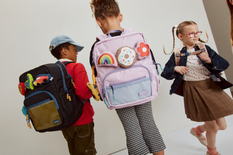Three children with colorful CALPAK backpacks against a plain background