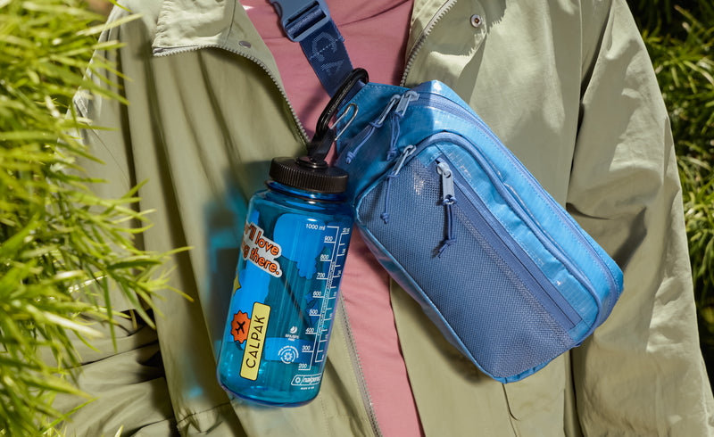 Model clipping on a water bottle on the CALPAK Terra Small Sling Bag in blue Glacier