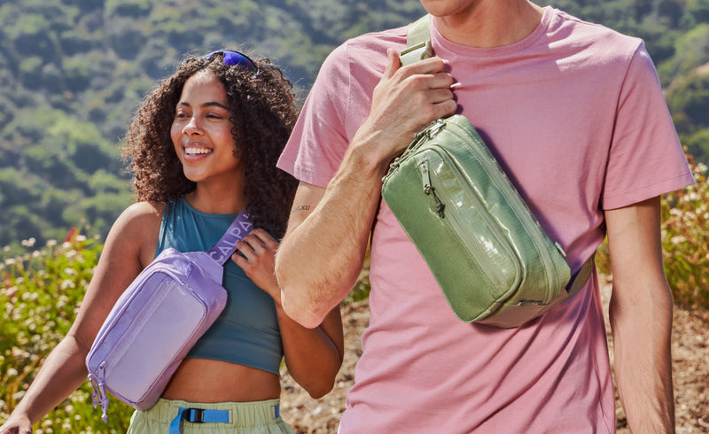 Models hiking wearing the CALPAK Terra Small Slings Bags in green Juniper and purple Amethyst