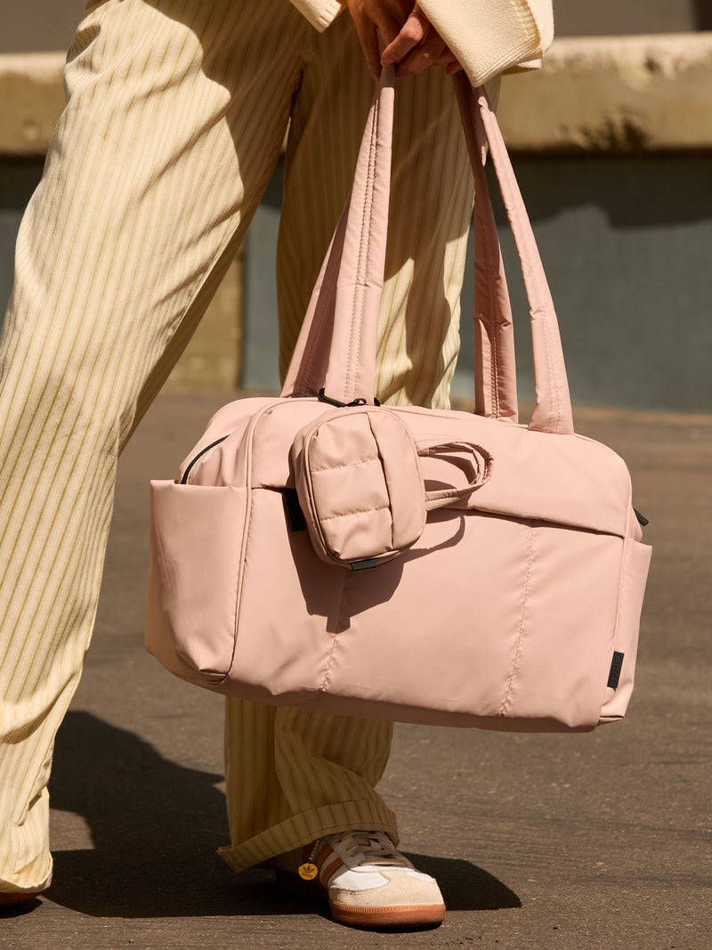 CALPAK Luka Duffel Key Pouch in pink Rose Quartz clipped onto the Luka Duffel in pink Rose Quartz being held by a model