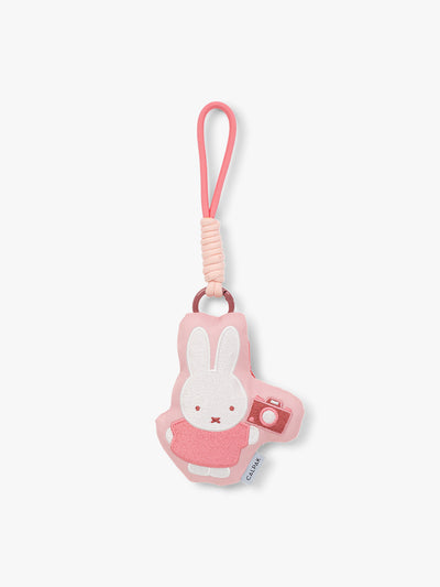 Plush Miffy x CALPAK Pluffy Bag Charm keychain with a pink border and Miffy holding a camera on a white background; APLF2501-MIFFY-MAKES-MEMORIES view 1