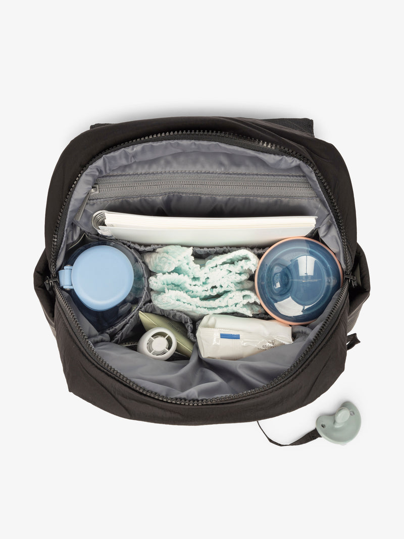 Inside view with baby items of the CALPAK Mini Diaper Backpack in Black on a white background