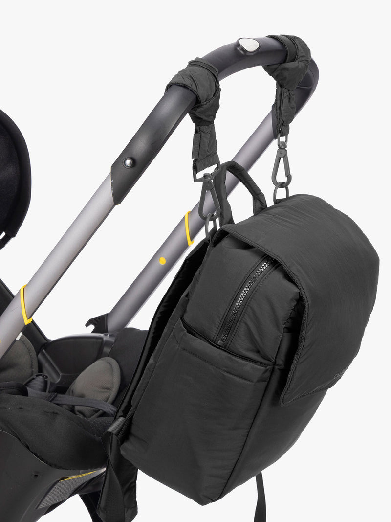 CALPAK Mini Diaper Backpack in Black strung on a stroller with stroller straps on a white background