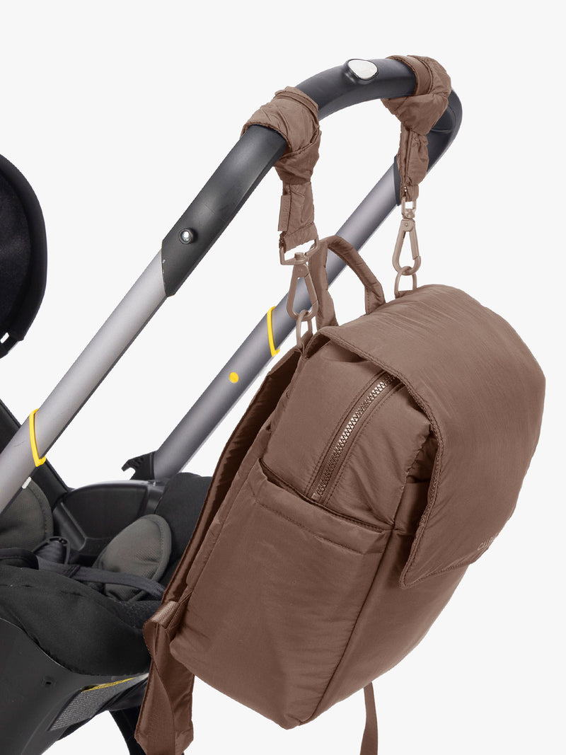 CALPAK Mini Diaper Backpack in brown Hazelnut hung on a stroller with straps on a white background