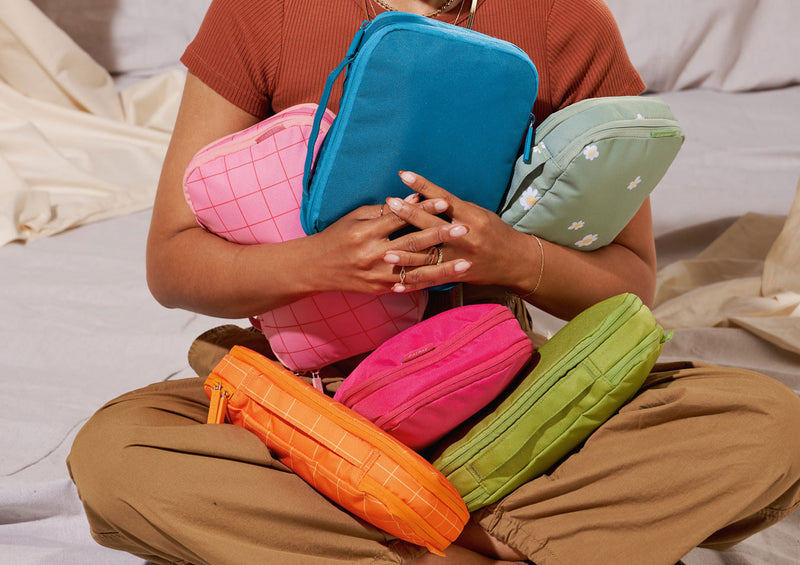 Model sitting with 6 CALPAK small compression packing cubes in a variety of bright colors and prints