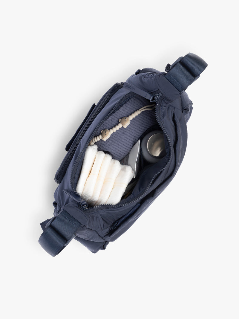 Top opened view with baby items in the CALPAK Crossbody Diaper Bag in blue Navy
