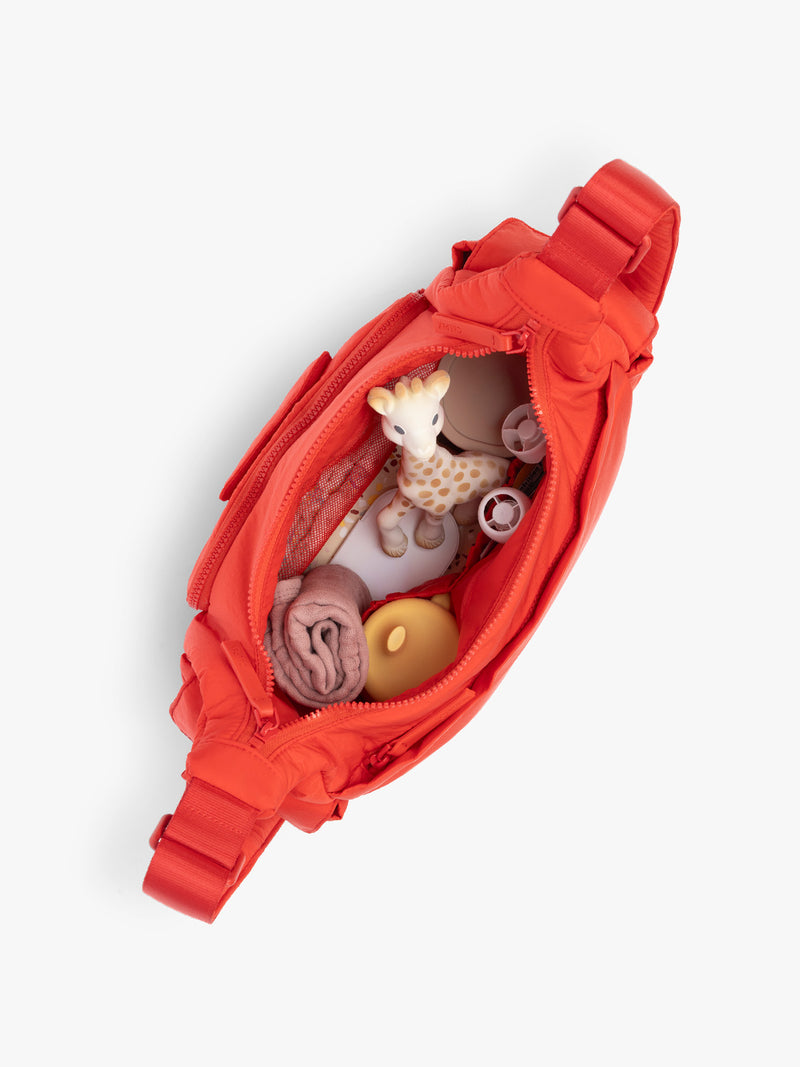 Top opened view with baby items inside CALPAK Crossbody Diaper Bag in red Tomato