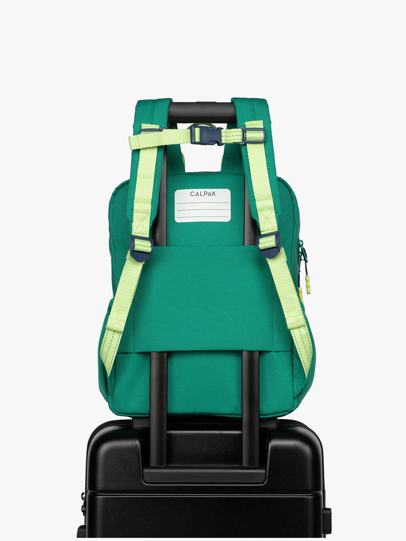 Back view of  luggage trolley sleeve and name tag of the Green CALPAK Kids Medium Backpack with lime green accents on a white background
