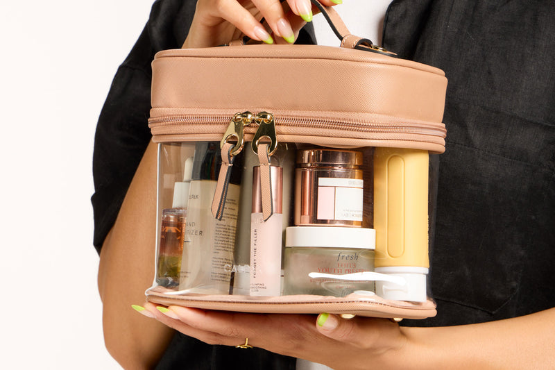 Model holding the CALPAK Clear Train Case in beige Caramel