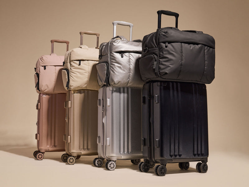 Set of CALPAK Ambeur suitcases and Luka duffels in various colors on a beige background