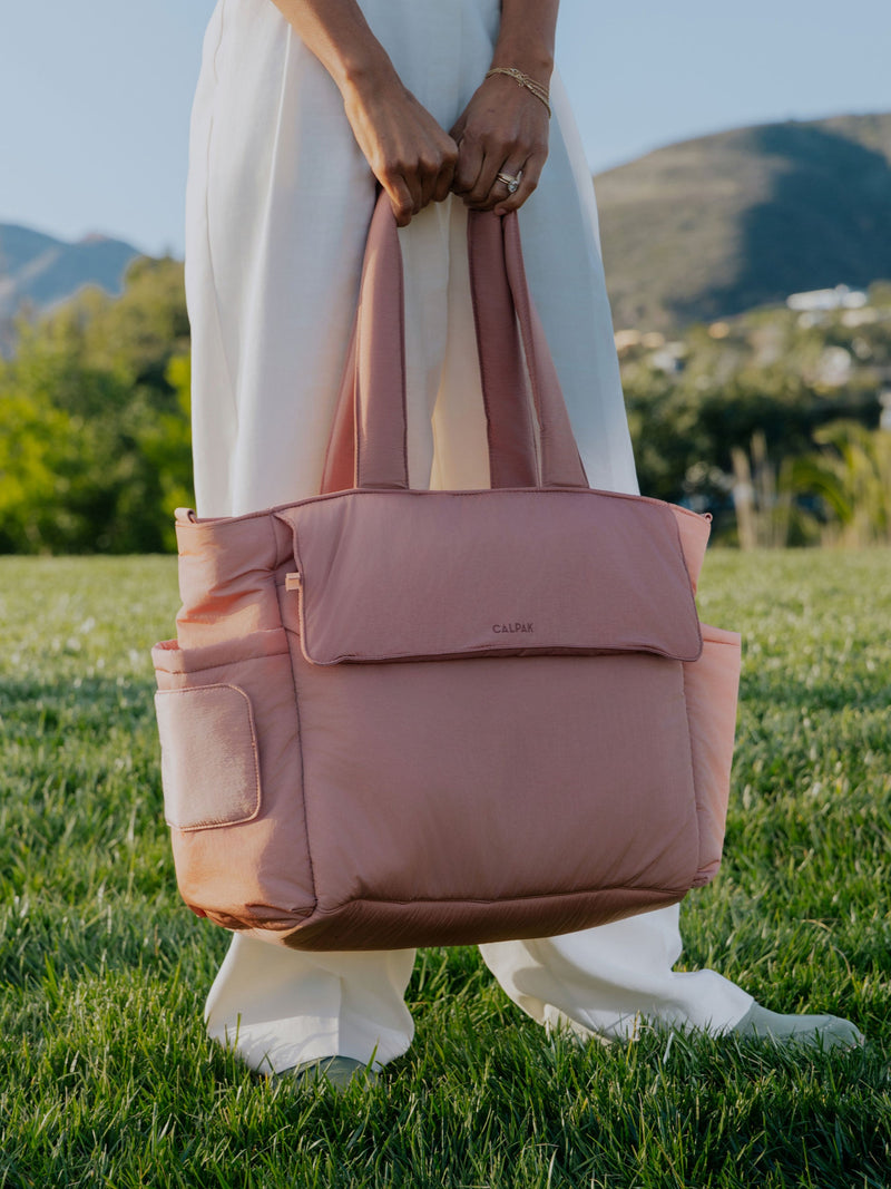 Woman stood in a green field by a hill-side holding a pink diaper tote bag with laptop sleeve