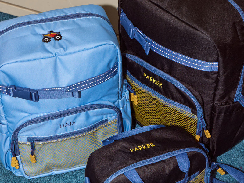 Two CALPAK Kids Collection backpacks, one blue and one black with 'Parker' personalization, on a textured surface.