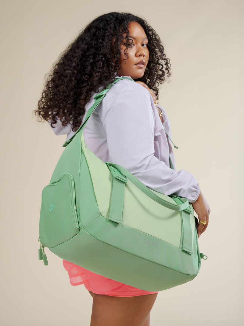 Model wearing adjustable shoulder strap of CALPAK Fit Gym Bag in sage green; TBF2401-SAGE, BTBF2401-SAGE