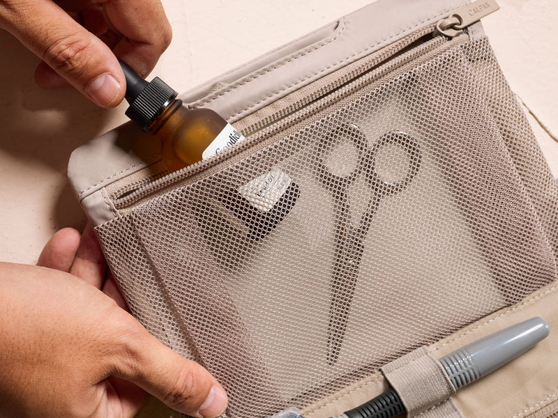 Model putting in toiletry into mesh pocket of the CALPAK beige FIt Hanging Dopp Kit