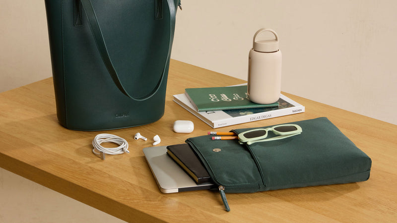 Green Haven 14" Laptop Tote with removeable laptop sleeve or insert on a wooden table with electronic items and books