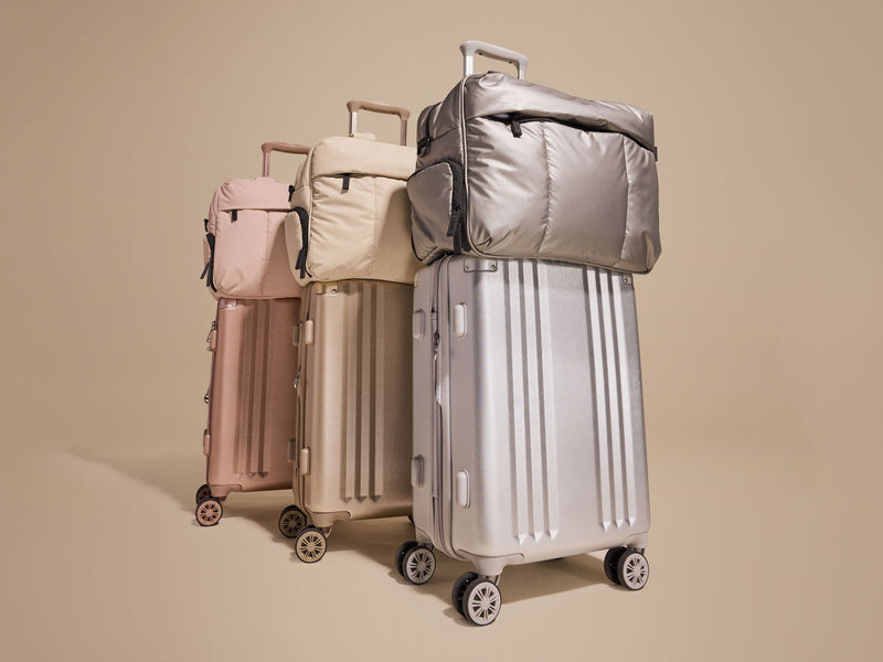 Set of CALPAK suitcases and bags in assortment of metallic colors on a beige background