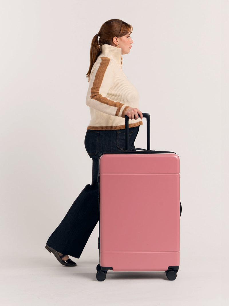 Model rolling with Hue Large hard shell Luggage in Mauve with handle extended and 360 spinner wheels.