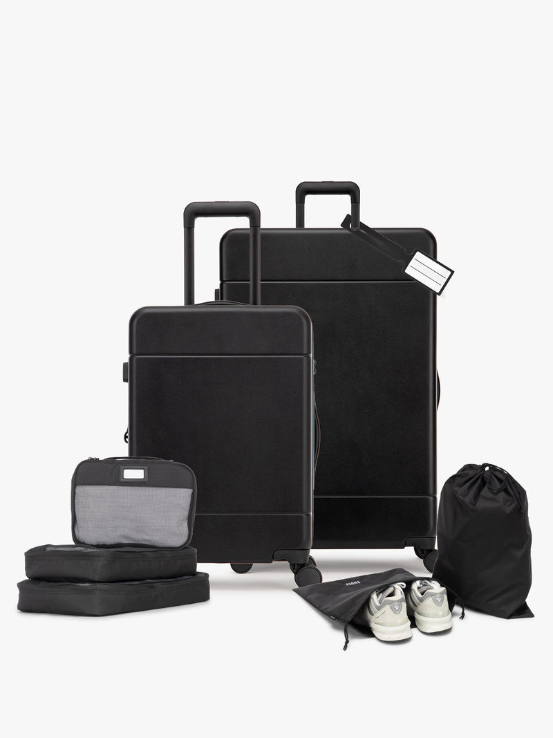 Opened CALPAK Hue Starter Bundle in Black that comes with Large and Carry On Luggage, Luggage Tag, Two Black Pouches, and Three Black Packing Cubes shown on a white background