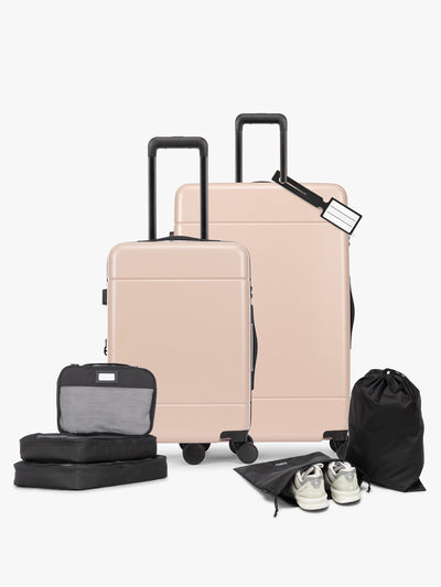 Opened CALPAK Hue Starter Bundle in light pink Rose Quartz that comes with Large and Carry On Luggage, Luggage Tag, Two Black Pouches, and Three Black Packing Cubes shown on a white background; LHU8000-ROSE-QUARTZ view 1