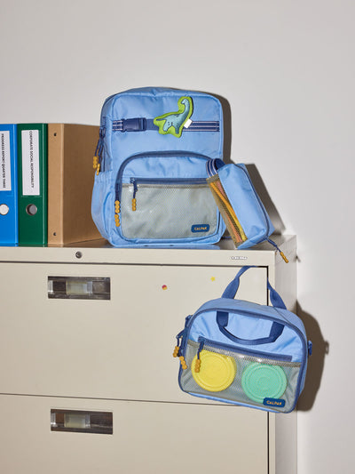 CALPAK Kids Collection Medium Kids Backpack Bundle in Blue that includes Kids Lunch Bag, Kids Pencil Case, blue and green Dinosaur Pluffy Bag Charm, and Set of 2 Ice Packs in a kid's room; BCKM5000-BLUE view 2