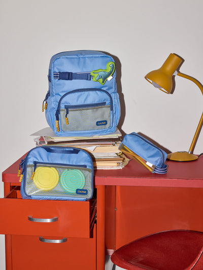CALPAK Kids Collection Small Kids Backpack Bundle in Blue that includes Kids Lunch Bag, Kids Pencil Case, blue and green Dinosaur Pluffy Bag Charm, and Set of 2 Ice Packs in a kid's room; BCKS5000-BLUE view 2