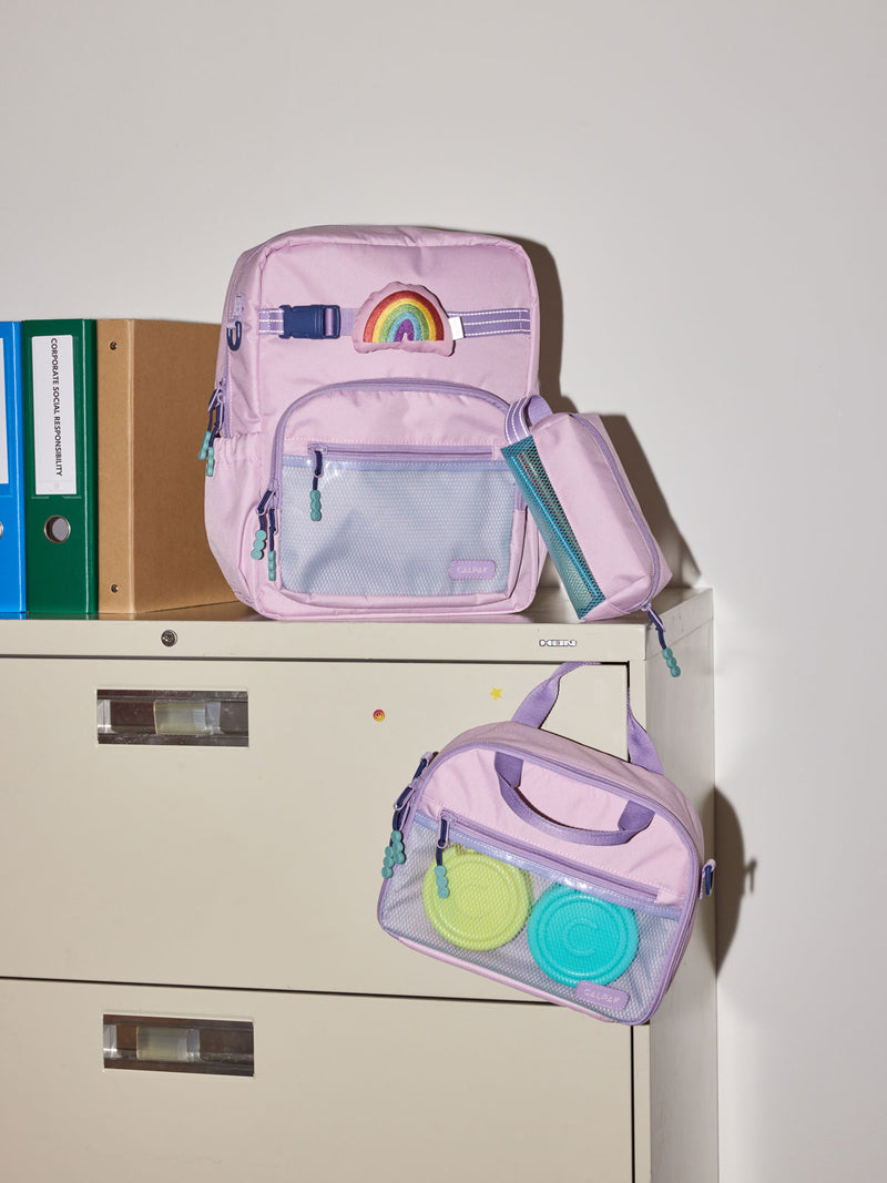 CALPAK Kids Collection Medium Kids Backpack Bundle in pink lavender Orchid Pink that includes Kids Lunch Bag, Kids Pencil Case, Rainbow Pluffy Bag Charm, and Set of 2 Ice Packs in a kid's room