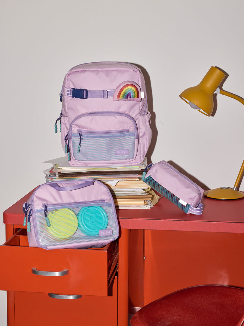 CALPAK Kids Collection Small Kids Backpack Bundle in pink lavender Orchid Pink that includes Kids Lunch Bag, Kids Pencil Case, Rainbow Pluffy Bag Charm, and Set of 2 Ice Packs in a kid's room