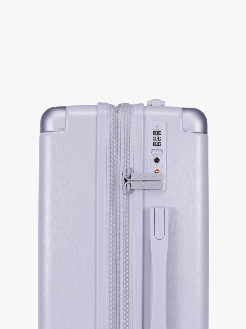 Side TSA lock of CALPAK Ambeur three piece luggage set in carry on, medium, and large sizes in light purple lavender with handles and spinner wheels on a white background
