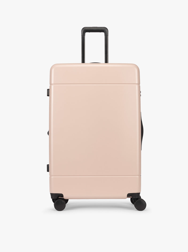 CALPAK Hue Large Luggage in light pink Rose Quartz with handle and wheels on a white background