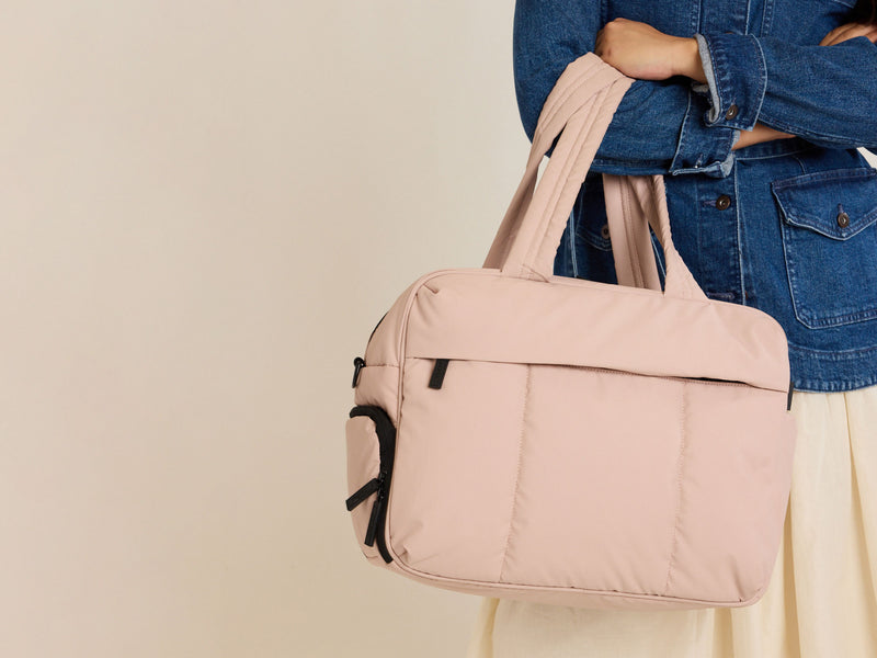 Person holding CALPAK pink Rose Quartz Luka Duffel against a beige background
