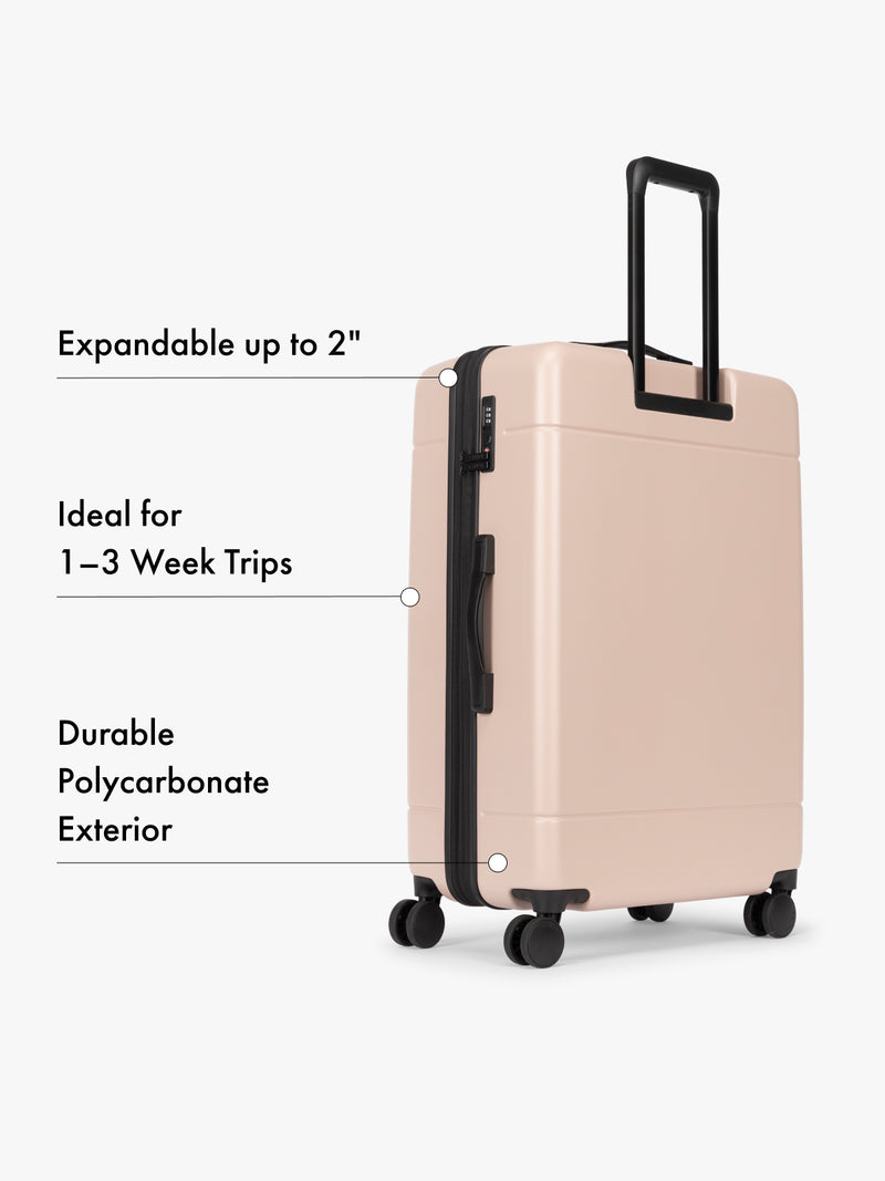 Backside of CALPAK Hue Large Luggage in light pink Rose Quartz with handle and wheels on a white background and features highlighted on white background