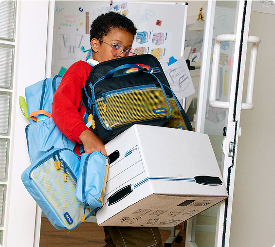 Child holding a box with CALPAK backpacks on a white background