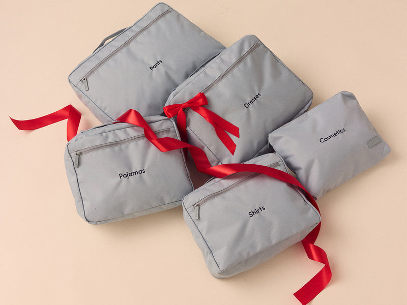 Set of blue CALPAK packing cubes with red ribbons on a beige background