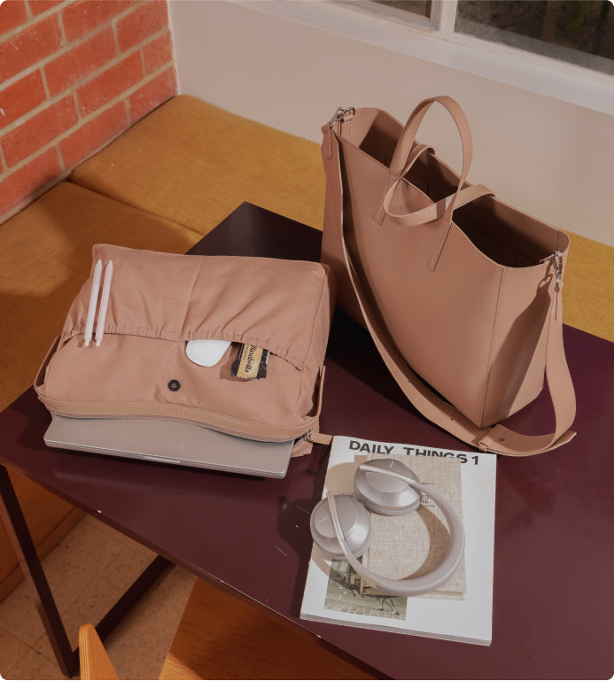 CALPAK Haven Laptop Tote Bag in light brown on table with headphones