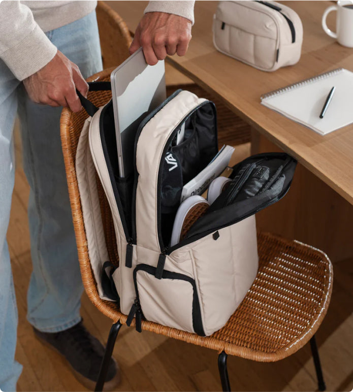 Model placing laptop in CALPAK Luka Laptop Backpack in Oatmeal