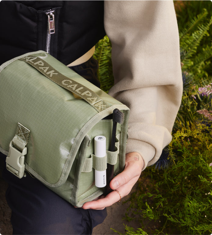 Model holding CALPAK Terra hanging toiletry bag in juniper green 