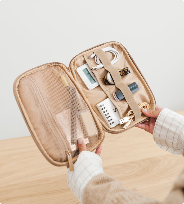 Model holding open CALPAK Tech Organizer in cheetah filled with tech accessories