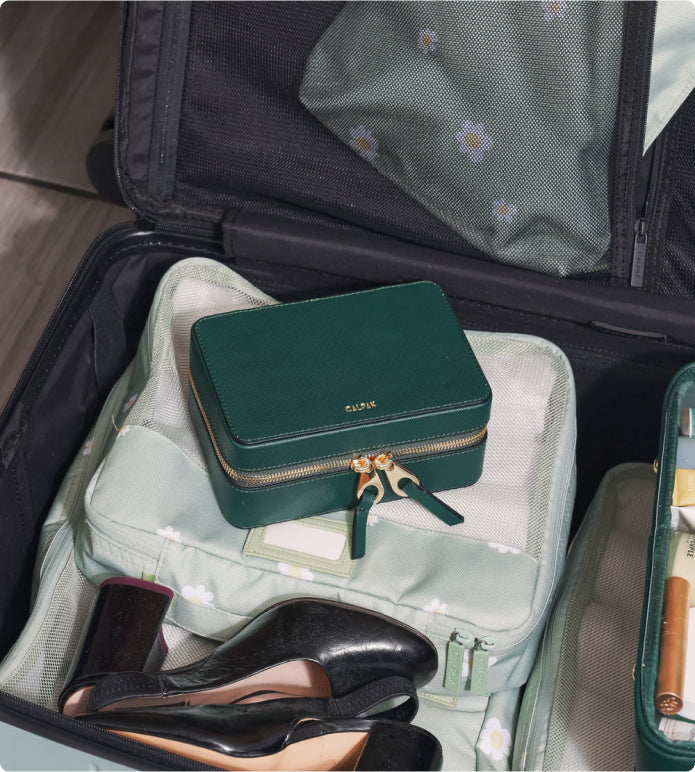 CALPAK emerald green jewelry case packed in black luggage with green packing cubes and shoes