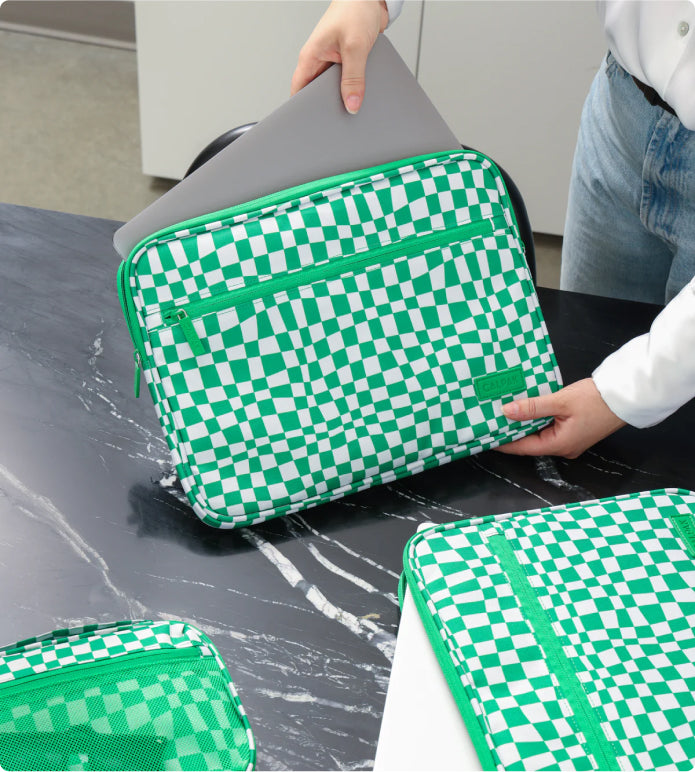 Model placing laptop into padded laptop sleeve in green checkboard print