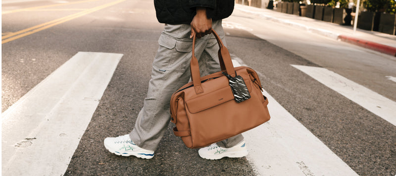 Model carrying a CALPAK brown Hue Duffel down a street 