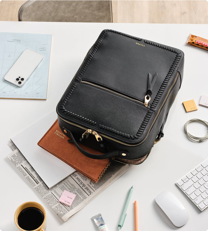 CALPAK Kaya Backpack in black on top of newspaper on desk