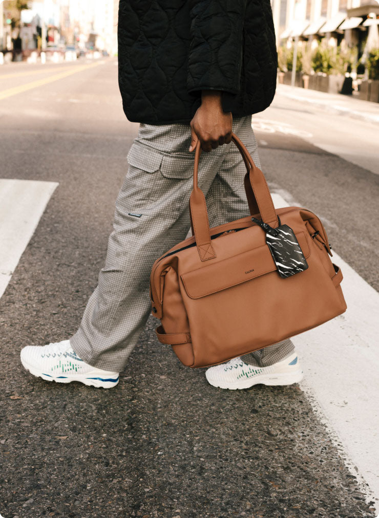 Model carrying a CALPAK brown Hue Duffel down a street 