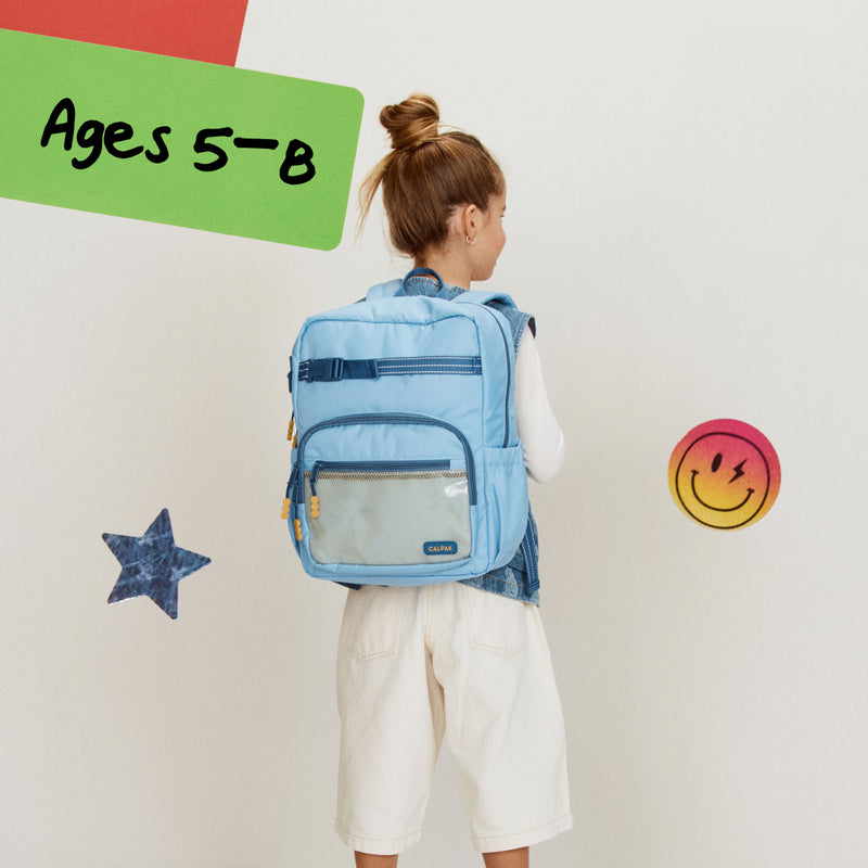 Child wearing the CALPAK Blue Medium backpack with decorative elements on a light gray background for ages 5-8