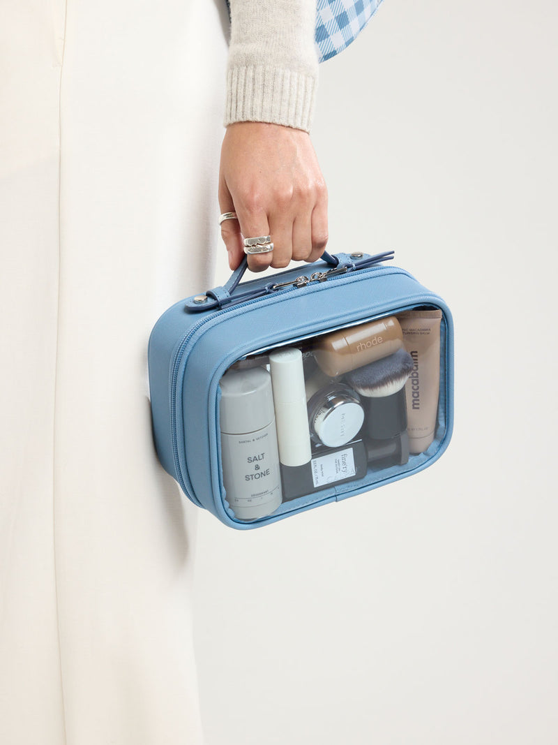 Person with CALPAK Small Clear Cosmetic Case in light blue French Blue with white and light blue gingham interior