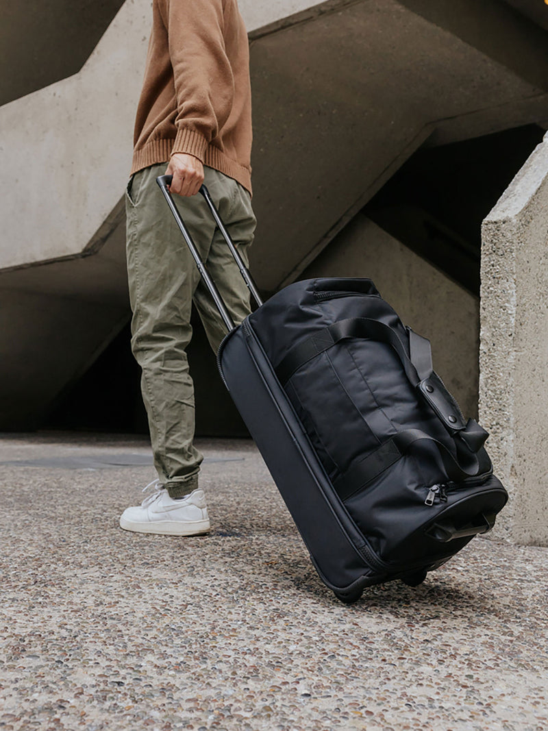 Model walking with Stevyn Large Rolling Duffel in black on cobblestone streets