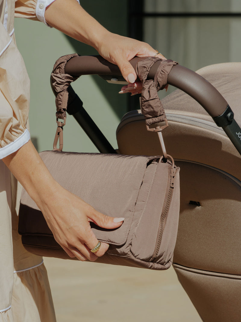 Stroller straps in hazelnut color, shown in a lifestyle setting securely attached to a stroller handle with a diaper bag hanging from them