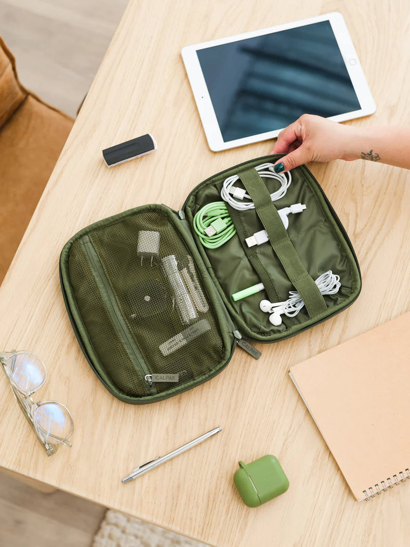 Model packing headphones, chargers and office supplies in CALPAK tech organizer in moss green